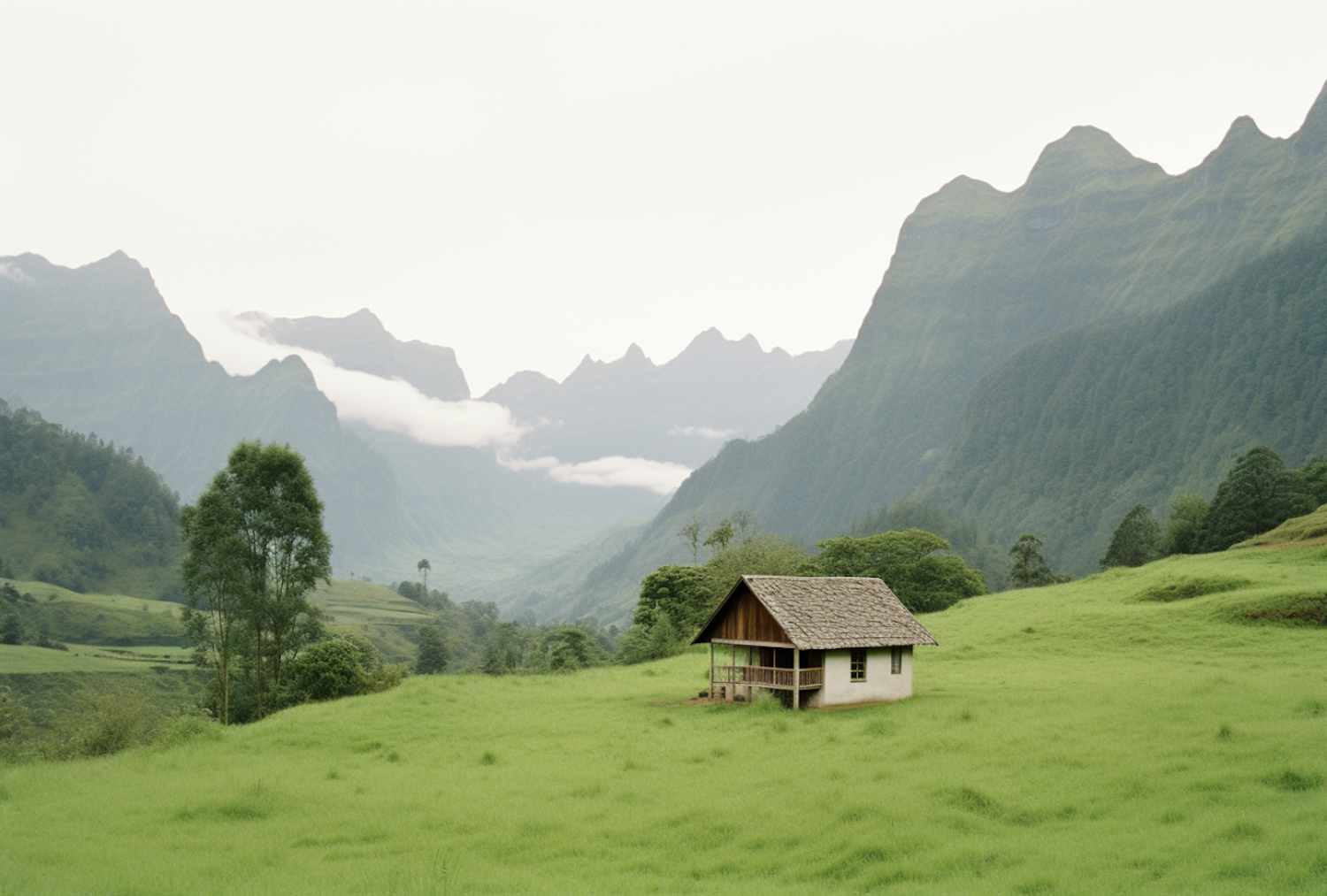 Small cottage with a wooden porch in a green meadow below misty mountains
